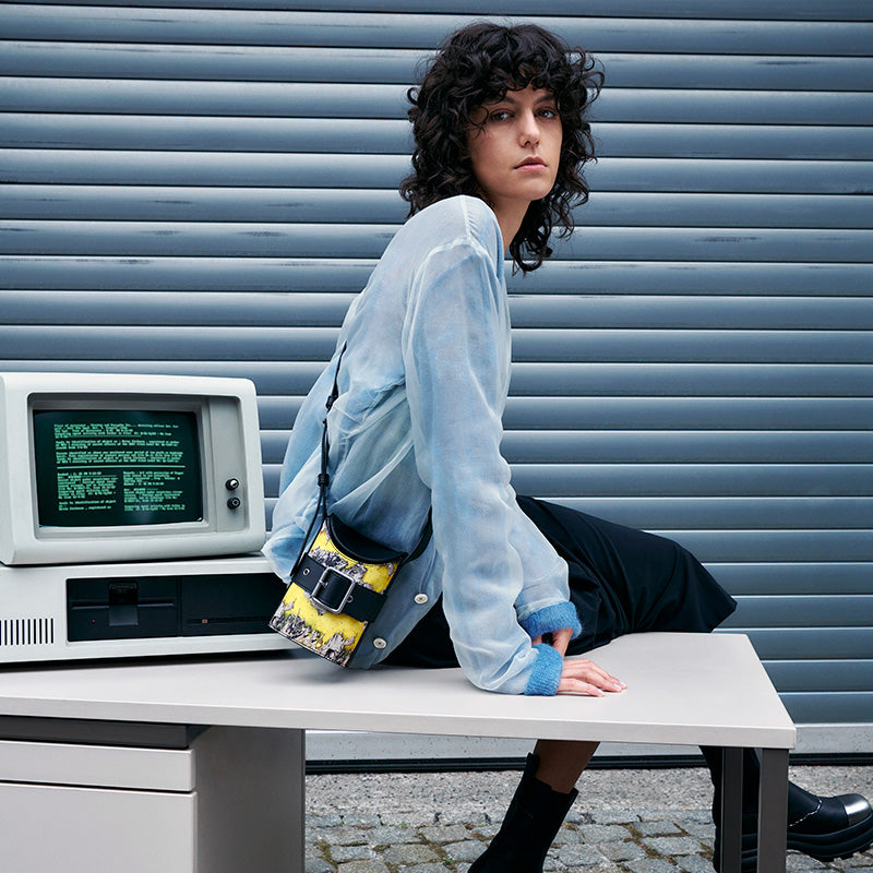 Woman sitting at table wearing both x CHARLES & KEITH multi-color bucket bag with vintage computer background