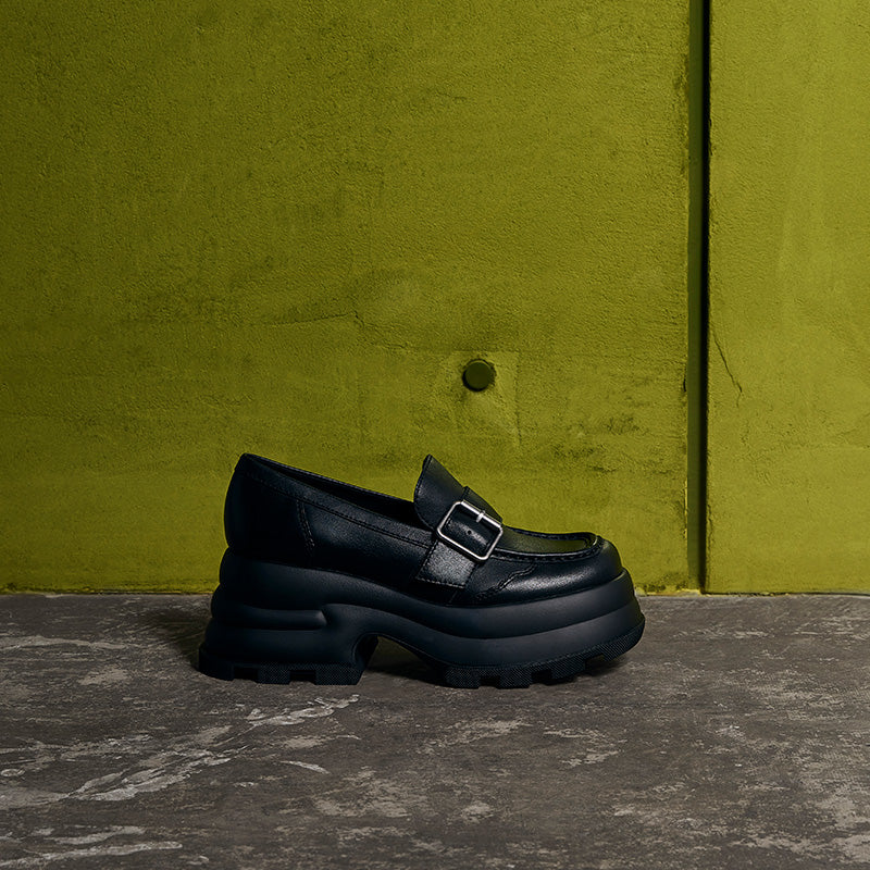 Black platform buckled loafer from CHARLES & KEITH with chunky sole against green wall background