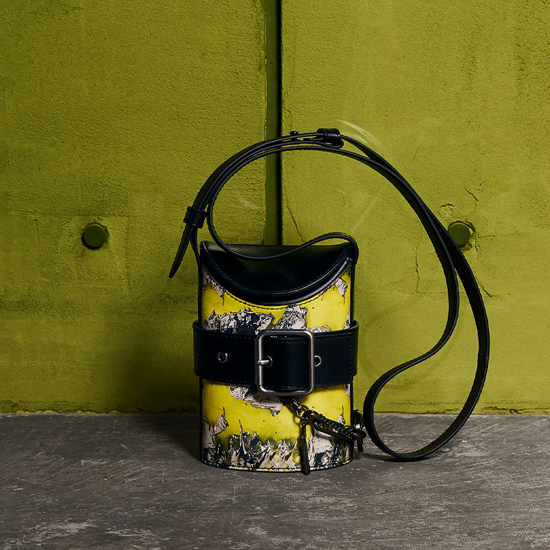 both x CHARLES & KEITH multi-color bucket bag with black strap and belt buckle on green background